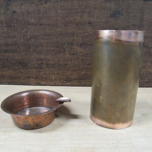 May include: Two copper metal containers. One is a small round bowl with a handle, and the other is a tall cylinder.