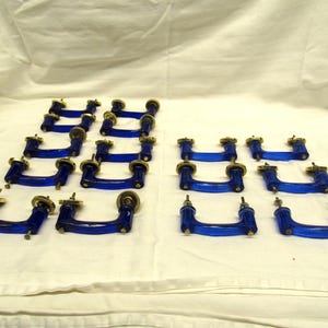 May include: A collection of blue glass cabinet pulls with brass-colored hardware. The pulls have a curved, U-shaped design. The hardware includes screws for mounting. The pulls are arranged on a white surface.