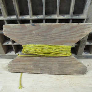 May include: A wooden spool with a yellow string wrapped around it. The spool is made of unfinished wood and has a simple design.