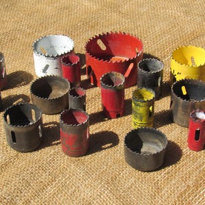May include: A collection of hole saws in various sizes and colors, including red, yellow, black, and white. The saws have toothed edges and cylindrical bodies, designed for cutting circular holes in wood or other materials.