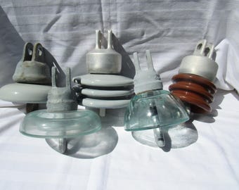 Op de afbeelding: Een verzameling vintage elektrische isolatoren. De isolatoren hebben glazen en keramische componenten in grijstinten, bruin en helder. Elke isolator heeft een metalen dop met een lus om op te hangen. Afmetingen in cm.