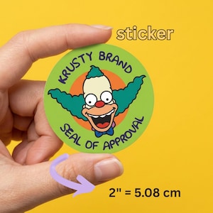 Puede incluir: Una pegatina redonda con Krusty el Payaso y el texto "KRUSTY BRAND SEAL OF APPROVAL" en verde y naranja. La pegatina tiene aproximadamente 5,08 cm de diámetro. El fondo es amarillo.