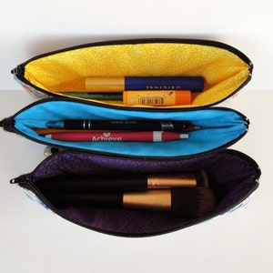May include: Three zippered pouches with different colored linings. The top pouch is yellow and contains a blue and yellow lip balm and a black and silver lip gloss. The middle pouch is blue and contains a red and silver pen and a black and silver pen. The bottom pouch is purple and contains a black makeup brush.