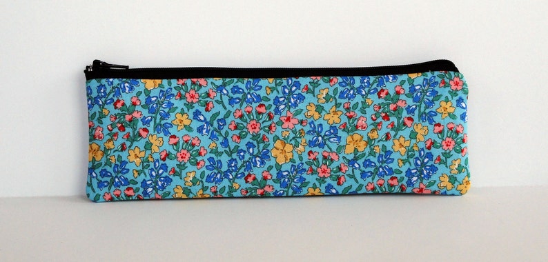 May include: A blue zippered pencil case with a floral print featuring pink, yellow, and blue flowers on a light blue background.