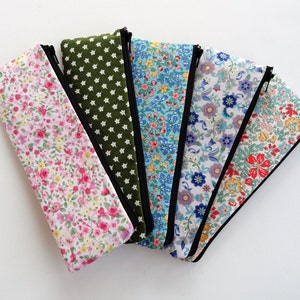May include: Six fabric pencil cases with different floral patterns. The cases are lined up in a row, with the green case at the top and the red case at the bottom.