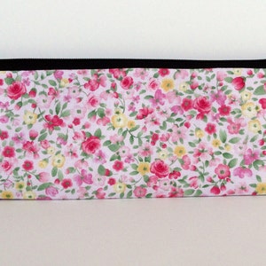 May include: A white zippered pouch with a floral print featuring pink, red, and yellow flowers on a white background.