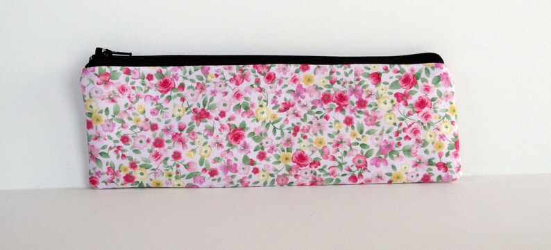 May include: A white zippered pouch with a floral print featuring pink, red, and yellow flowers on a white background.
