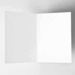 May include: An open, blank greeting card with a textured, off-white cover. The inside pages are bright white, creating a contrast with the cover. The card is displayed against a plain, light gray background.