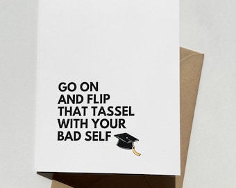 May include: A white graduation card with black text that reads "GO ON AND FLIP THAT TASSEL WITH YOUR BAD SELF." A small illustration of a graduation cap with a yellow tassel is on the right. The card rests on a brown envelope.