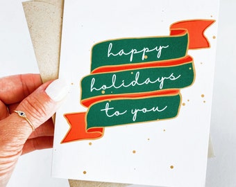 Pode incluir: Um cartão branco com uma faixa verde e vermelha que diz "felizes festas para você". A faixa tem detalhes dourados e há pontos dourados espalhados pelo cartão.