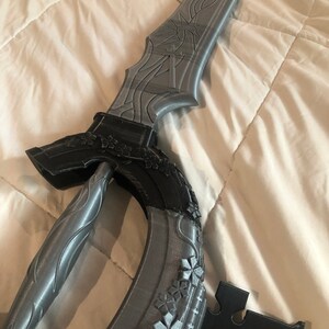 May include: A gray 3D printed sword with intricate details and a black handle. The sword has a curved blade and a decorative design on the hilt.