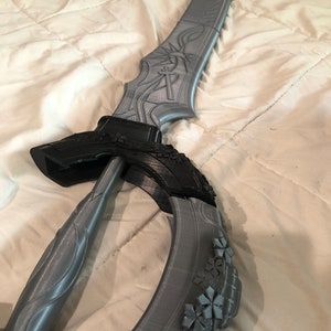 May include: A gray 3D printed sword with a black handle and intricate details. The sword is curved and has a floral design on the blade.