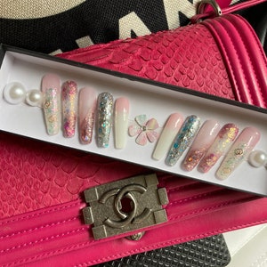May include: A set of 10 false nails with a white, pink, and blue ombre design. The nails are decorated with glitter, small flowers, and pearls.