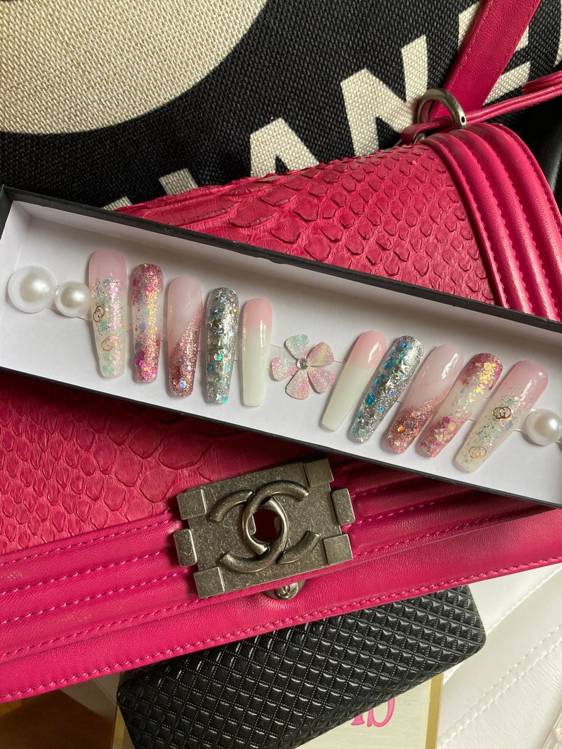 May include: A set of 10 false nails with a white, pink, and blue ombre design. The nails are decorated with glitter, small flowers, and pearls.