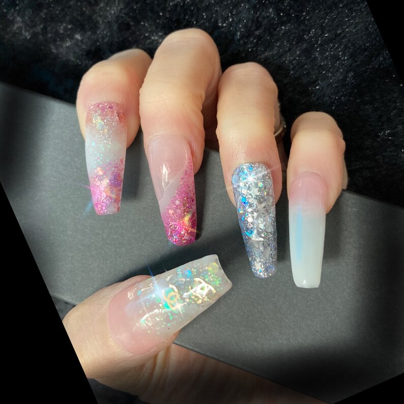 May include: Close-up of long, white, pink, and silver glitter nail tips. The nails are long and have a coffin shape. The glitter is applied in a gradient pattern, with the darkest glitter at the base of the nail and the lightest glitter at the tip.