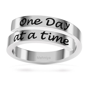 Könnte beinhalten: Silberring mit der Gravur "one day at a time". Der Ring ist ein schlichtes Band mit leicht gebogener Form.