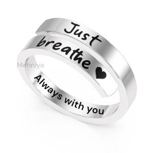 Może przedstawiać: Srebrny pierścionek z czarnymi napisami "Just breathe" i "Always with you". Zawiera również małe czarne serce. Pierścionek ma unikalny, owijający się design.