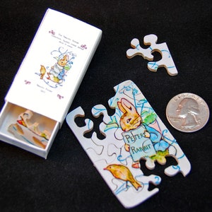 以下が含まれることがあります： ビートリックス・ポターの子供向けの本からピーターラビットをフィーチャーした小さな木製ジグソーパズル。パズルはマッチ箱サイズの箱に入っていて、本のタイトルと著者が箱に印刷されています。パズルピースは箱の周りに散らばっています。