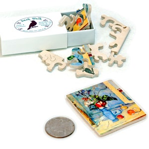 May include: A small wooden jigsaw puzzle with a colorful still life painting of a vase with flowers and fruit. The puzzle pieces are scattered around a white box with the text "bark walk" and a black bird logo. A US quarter is included for scale.