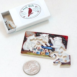 May include: A small wooden puzzle featuring a white cat with a red background. The puzzle is made up of several pieces and is in the process of being assembled. The puzzle is in a matchbox-sized box with a red bird and the words "Bark Walk" on the label.