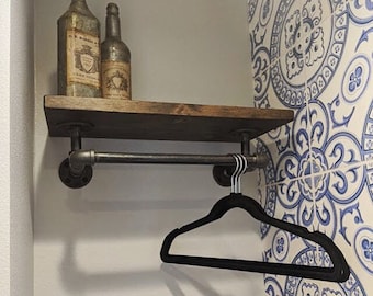 May include: A dark brown wooden shelf with black metal pipe supports and a black metal pipe rod. The shelf is mounted to a white wall with blue and white patterned tile. A black velvet hanger is hanging from the rod.