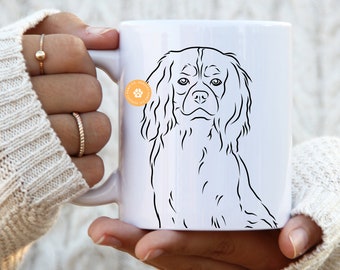 May include: White ceramic mug with a black line drawing of a Cavalier King Charles Spaniel dog. The mug has a handle and a paw print logo.