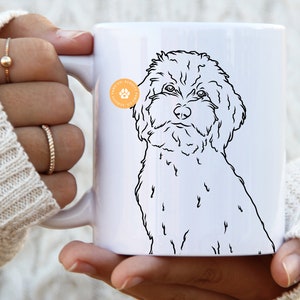 May include: White ceramic mug with a black line drawing of a small, fluffy dog. The dog is looking directly at the viewer. The mug has a black paw print with the text "Pawsitive Prints" in a circle on the side.