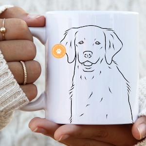 Puede incluir: Taza de cerámica blanca con un dibujo de línea negra de un Golden Retriever. La taza tiene una pequeña pegatina con una huella de pata en el lateral.