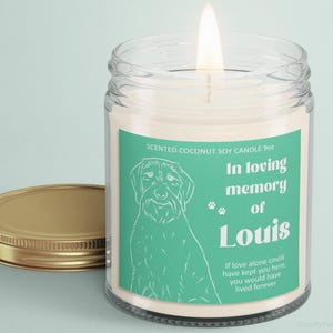 May include: A lit scented soy candle in a glass jar with a gold lid. The label features a dog illustration and the text "In loving memory of Louis". The candle is 9oz.