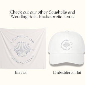 May include: White banner with the text "Seashells and Wedding Bells" and a seashell graphic. White baseball cap with the same text and graphic.