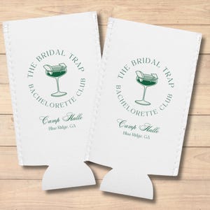 Könnte beinhalten: Zwei weiße Getränkedosenkühler mit grünem Text und einer grünen Illustration eines Cocktailglases. Der Text lautet "The Bridal Trap Bachelorette Club" und "Camp Halle Blue Ridge, GA".