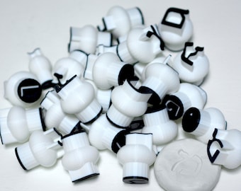 May include: A pile of white plastic stamps with black Hebrew letters. The stamps are arranged in a random order. There is a small piece of clay with a Hebrew letter imprinted on it.