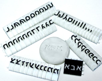 May include: White plastic tiles with black lettering spelling out different words in a fictional alphabet. The words include "JJAADOOONNN", "JJJAAADIIIII", "AACA", "YXTTVVCCCAA", and "ACA".