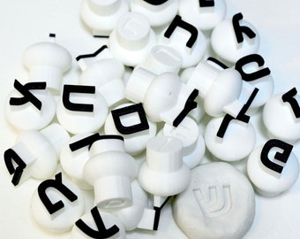 May include: A collection of white plastic Hebrew alphabet letter stamps with black lettering.