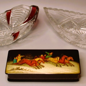 May include: A small wooden box with a black lacquered finish and a painted scene of a horse-drawn sleigh with people riding in a snowy landscape. The box is sitting on a white surface next to two clear glass bowls.