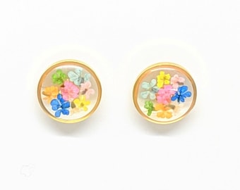 May include: A pair of gold stud earrings with a clear resin setting filled with colourful pressed flowers. The earrings are small and delicate, perfect for everyday wear.