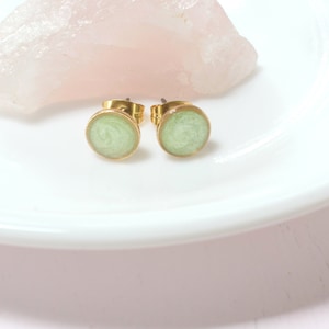 May include: A pair of gold stud earrings with a light green circular resin inlay.