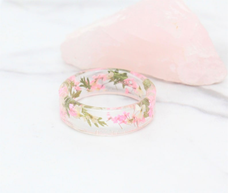 May include: A clear resin ring with pink and green pressed flowers embedded inside.