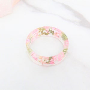 May include: A clear resin ring with pink and green pressed flowers embedded inside.
