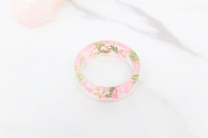 May include: A clear resin ring with pink and green pressed flowers embedded inside.