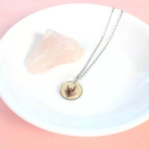 May include: A silver chain necklace with a round pendant featuring a pressed dried flower in a clear resin setting.