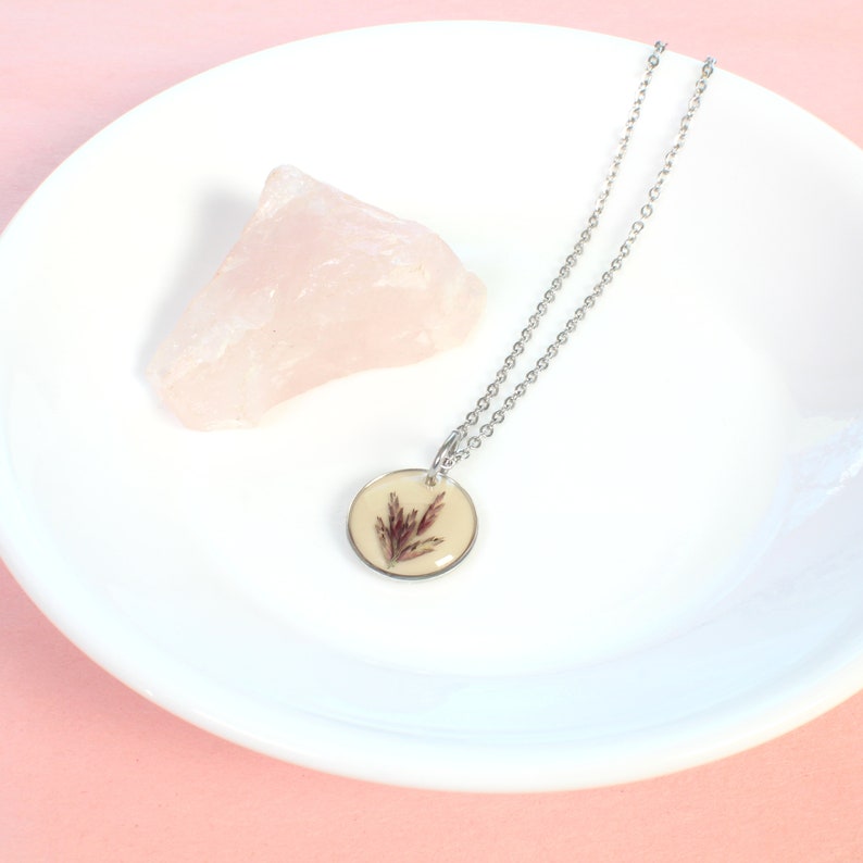 May include: A silver chain necklace with a round pendant featuring a pressed dried flower in a clear resin setting.