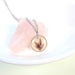 May include: A silver chain necklace with a round pendant featuring a pressed dried flower in a clear resin setting.