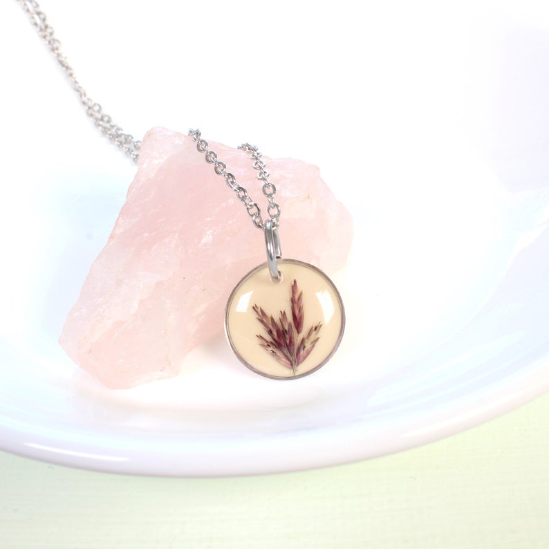 May include: A silver chain necklace with a round pendant featuring a pressed dried flower in a clear resin setting.