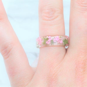 May include: A clear resin ring with pink and green pressed flowers embedded inside.