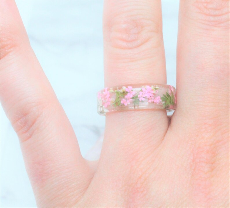 May include: A clear resin ring with pink and green pressed flowers embedded inside.