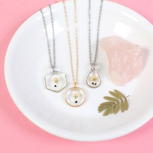 May include: Three delicate necklaces with silver and gold chains and clear resin pendants featuring pressed flowers. The pendants are a hexagon, a circle, and a teardrop shape.