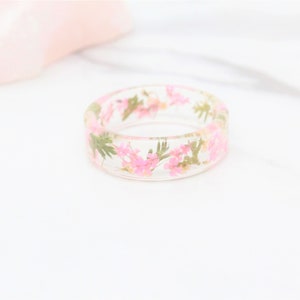 May include: A clear resin ring with pink and green pressed flowers embedded inside.
