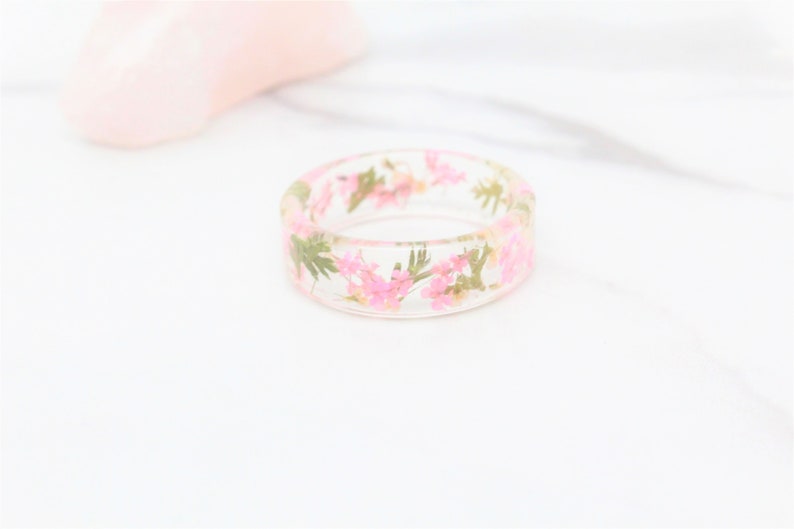 May include: A clear resin ring with pink and green pressed flowers embedded inside.