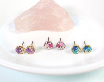 May include: Three pairs of hexagonal stud earrings with gold settings. Each pair features a different colour of pressed flowers: purple and pink, pink and white, and blue.